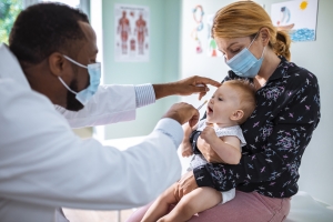 Close up of a pediatrician examining a baby patient being held by its mother