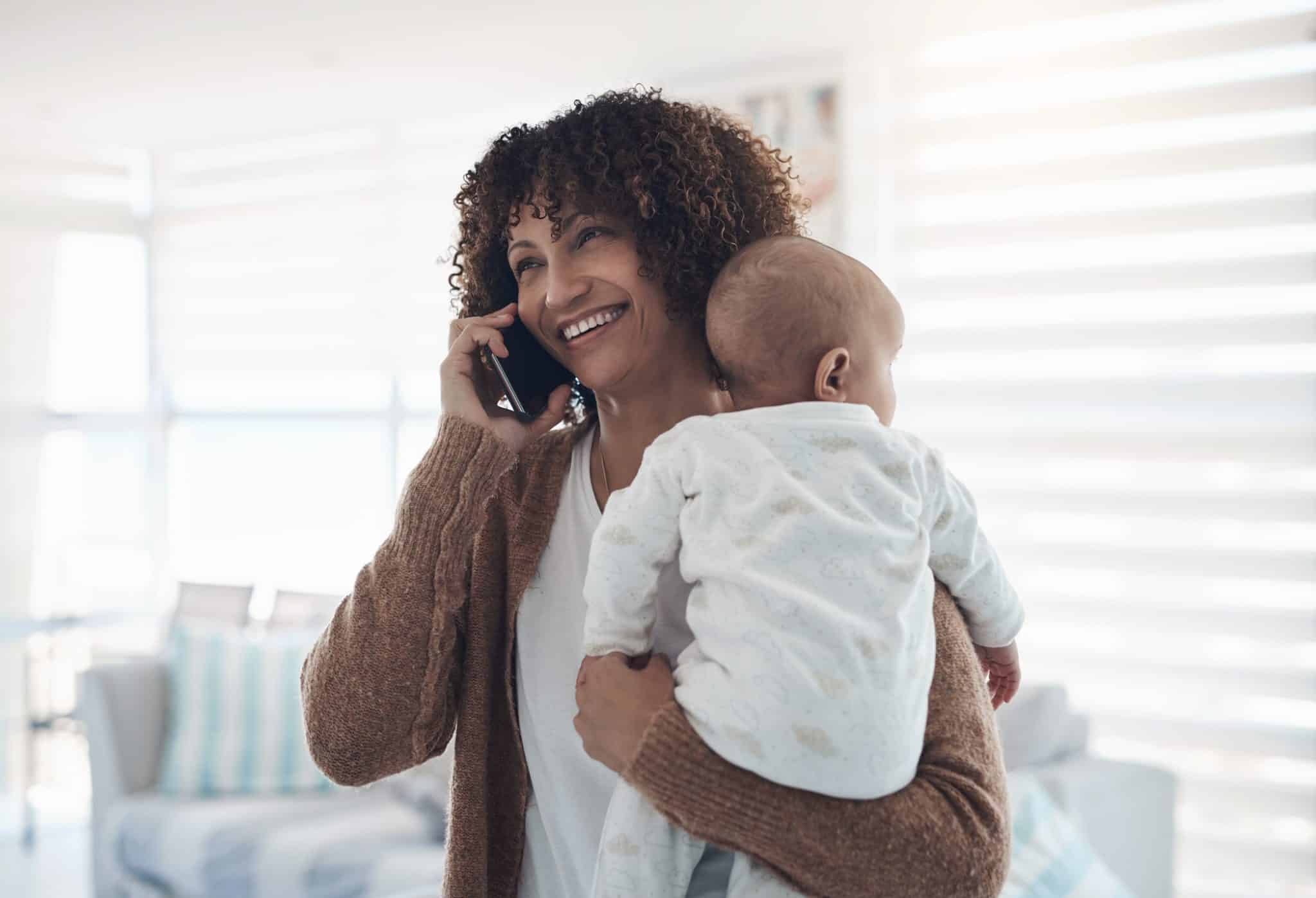 Shot of a young woman using a smartphone while carrying her adorable baby girl at home Woman calling a pediatrician to schedule an appointment for her baby.