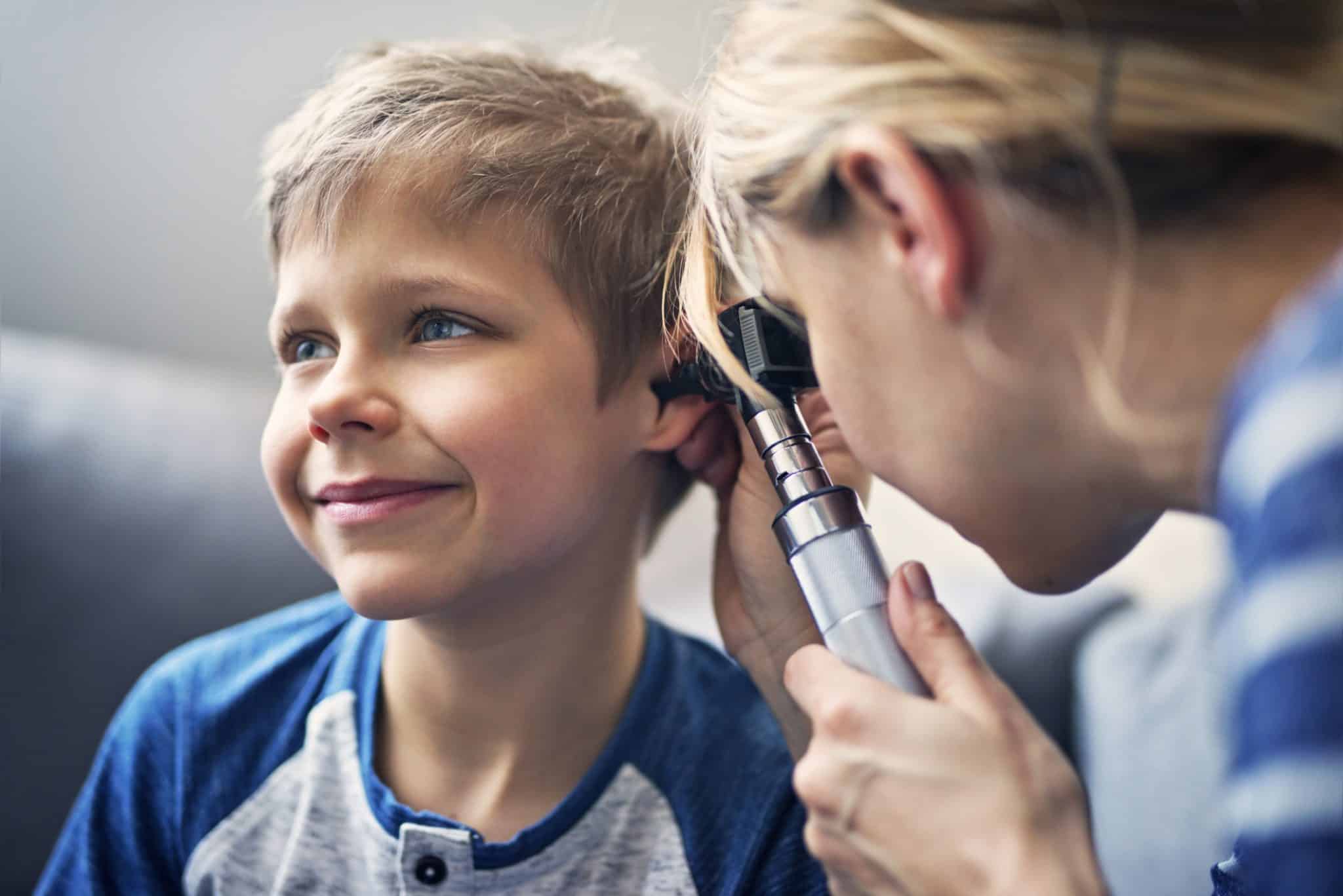 Happy little boy having ear exam Young boy smiling while getting his ears examined during a pediatric appointment.