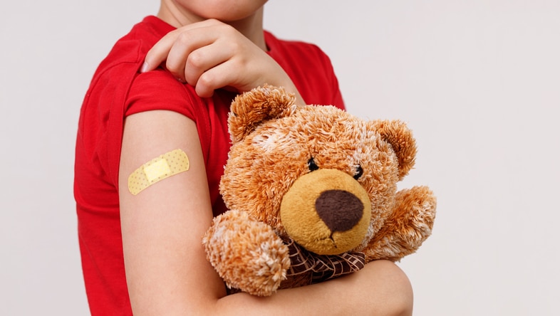 Child holding a bear showing off the bandage on his arm after he got is vaccine shot.