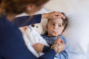 sick young boy getting his temperature taken by his caring mother while he is laying in bed.