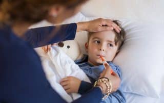 sick young boy getting his temperature taken by his caring mother while he is laying in bed.