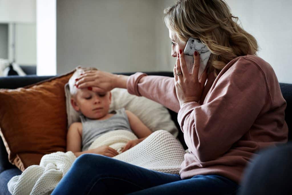mother feeling sick son's forehead as she calls to schedule a pediatric sick visit